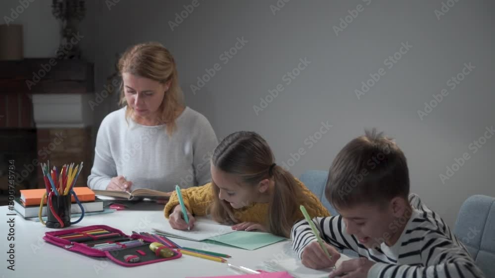 Tutor teaching two schoolchildren at home. Caucasian boy and girl doing homework. Kids writing in exercise books and young woman giving tasks. Education, intelligence, elementary school. Tutor teaching two schoolchildren at home. Caucasian boy and girl doing homework. Kids writing in exercise books and young woman giving tasks. Education, intelligence, elementary school.