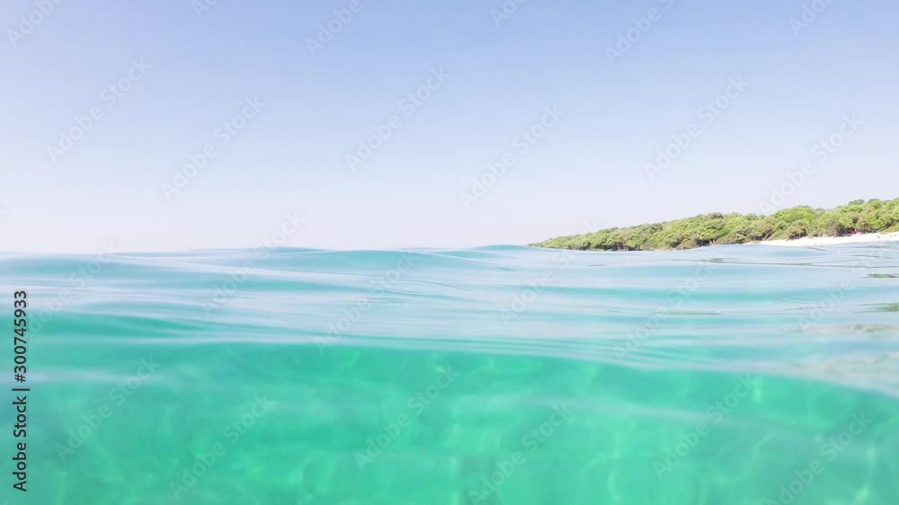 SLOW MOTION Steady shot above and underwater at sea water surface with distant mediterranean beach in background SLOW MOTION Steady shot above and underwater at sea water surface with distant mediterranean beach in background