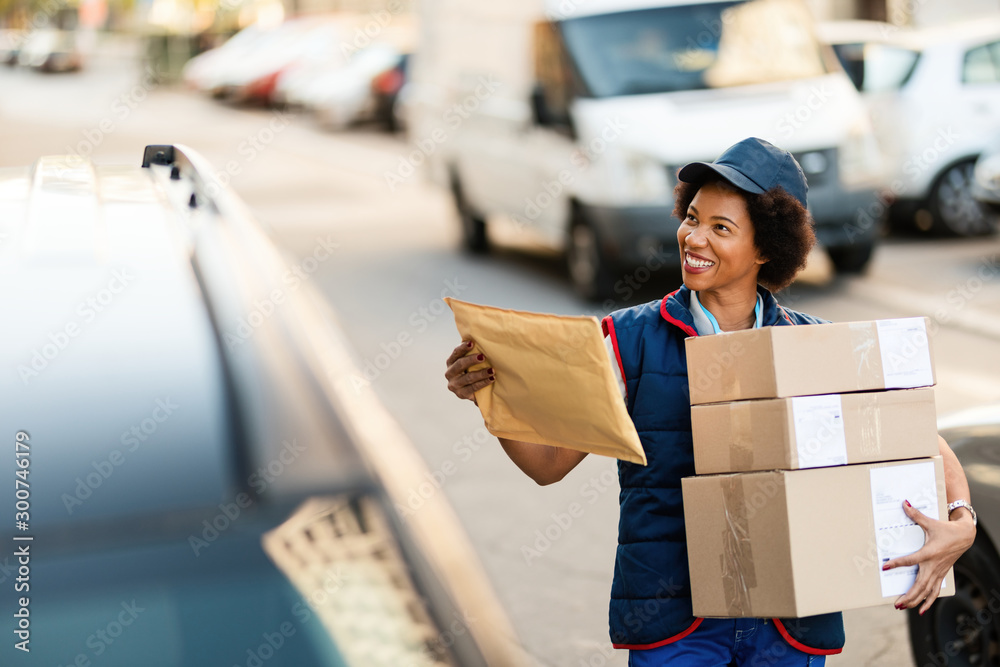 © Drazen - Happy black postal worker delivering packages in the city. © Drazen - Happy black postal worker delivering packages in the city.