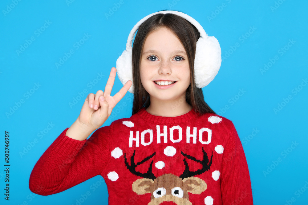 Little girl in christmas sweater and earmuffs on blue background Little girl in christmas sweater and earmuffs on blue background