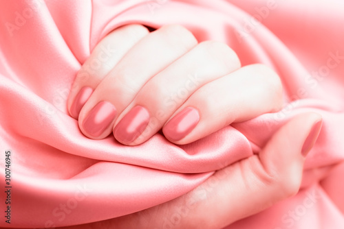 Female hand with pale pink manicure on a pink background