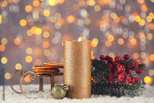 Christmas candle with red berries, sleigh and dry oranges on blurred background