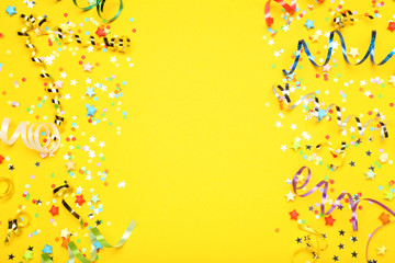 Colorful ribbons with paper stars and confetti on yellow background