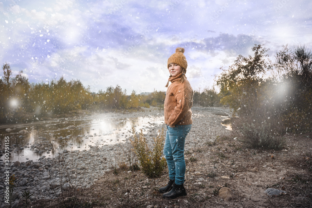 Beautiful blond girl in a wool sweater and a cap. Beautiful autumn landscape with a river in the background..