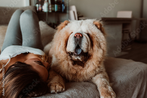 .Pretty young woman playing and sharing her time at home with her chow chow dog. Lying on the couch relaxed and carefree. Lifestyle
