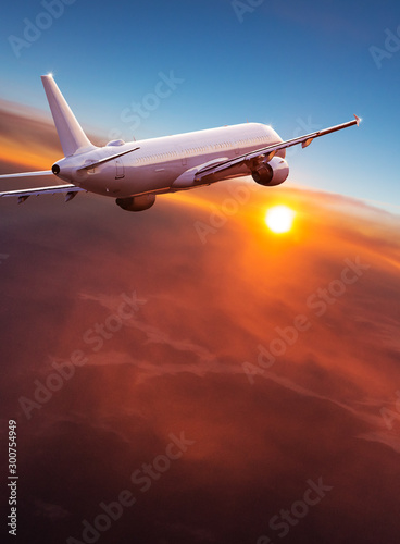 Commercial airplane flying above dramatic clouds during sunset.