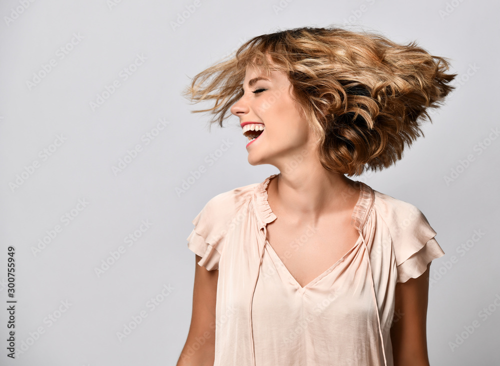 young woman in a beige short-sleeved satin blouse shakes her head with her hair. The concept of joy, happiness, joy, fun. - obrazy, fototapety, plakaty 