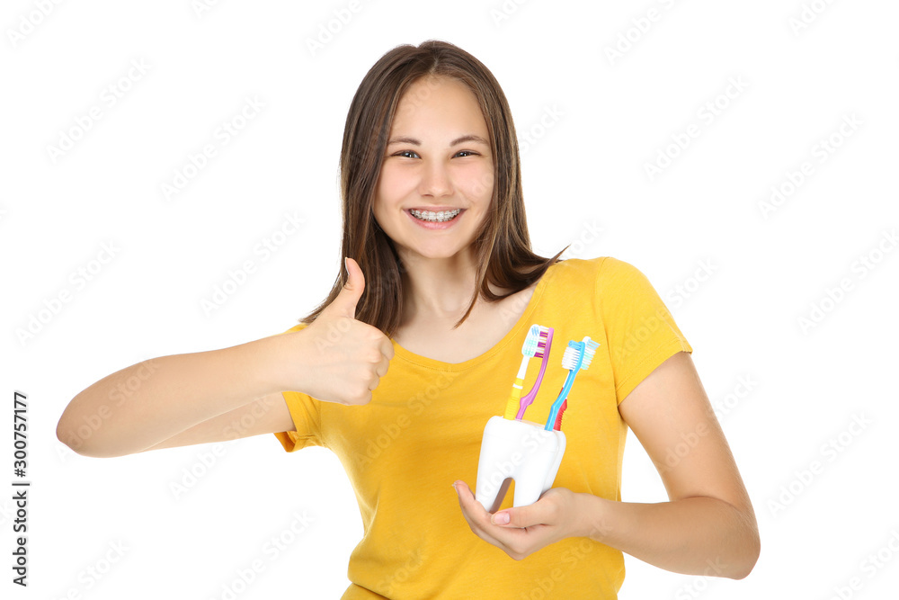 Young girl with dental braces holding toothbrushes and showing thumb up on white background Young girl with dental braces holding toothbrushes and showing thumb up on white background