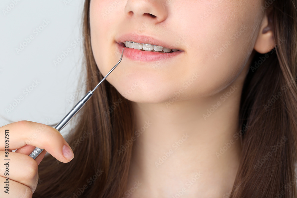 Young girl with dental braces holding dentist tool on grey background Young girl with dental braces holding dentist tool on grey background