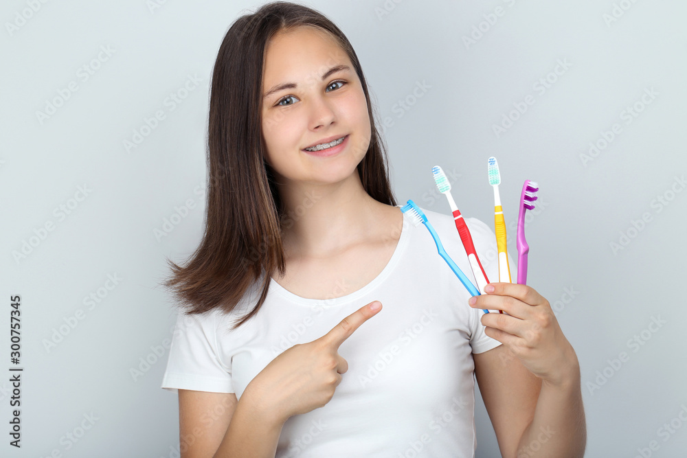 Young girl with dental braces holding toothbrushes on grey background Young girl with dental braces holding toothbrushes on grey background