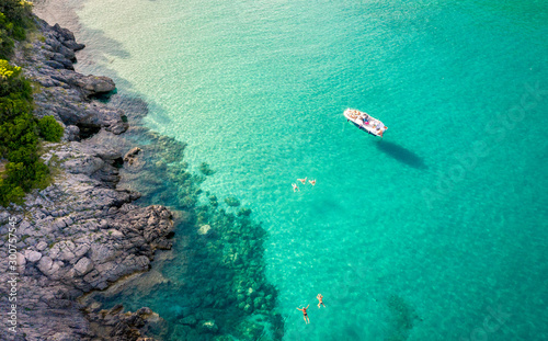 Aerial view of Trsteno beach in Montenegro, near Budva, a boat in a beautiful bay with a rocky shore, blue water, people bathe in clear water photo