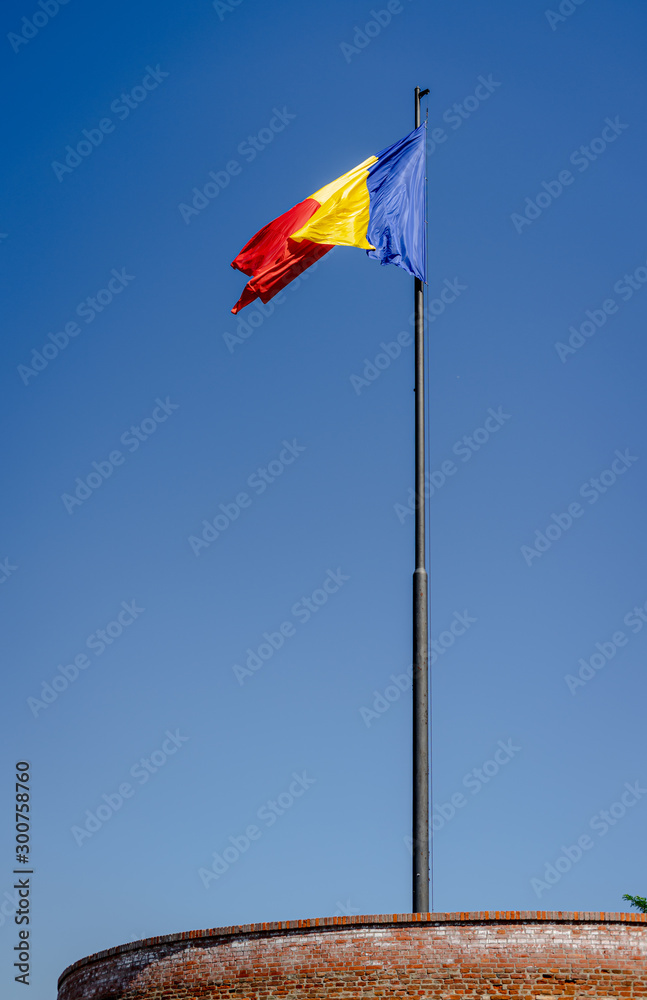 Romanian flag in the wind with the blue sky on the background. Alba Iulia citadel tower. Daylight, strong wind, historic, political.