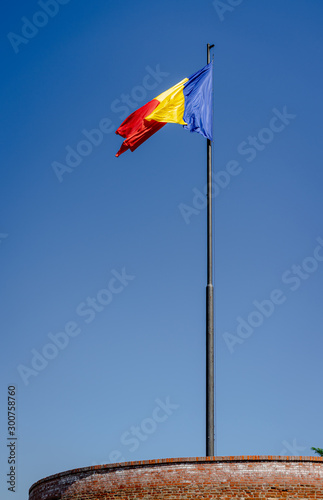 Romanian flag in the wind with the blue sky on the background. Alba Iulia citadel tower. Daylight, strong wind, historic, political.