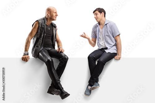 Young man talking to a punk in leather clotes and sitting on a panel