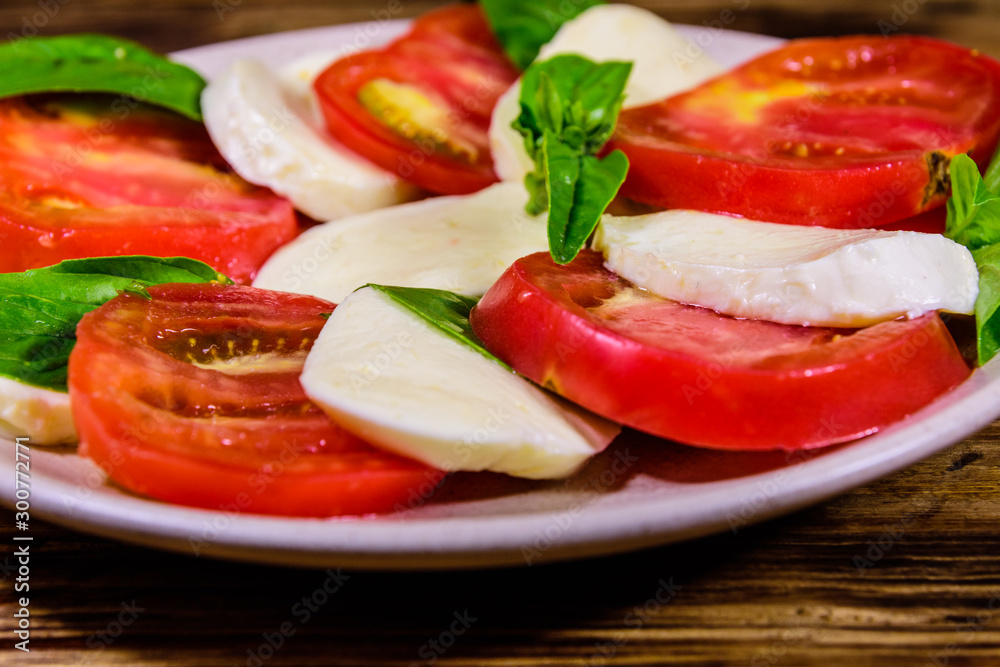 Plate with caprese salad (italian salad with cherry tomatoes, mozzarella cheese and basil leaves) on wooden table Plate with caprese salad (italian salad with cherry tomatoes, mozzarella cheese and basil leaves) on wooden table