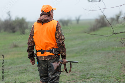 Hunting period, autumn season open. A hunter with a gun in his hands in hunting clothes in the autumn forest in search of a trophy. A man stands with weapons and hunting dogs tracking down the game.	