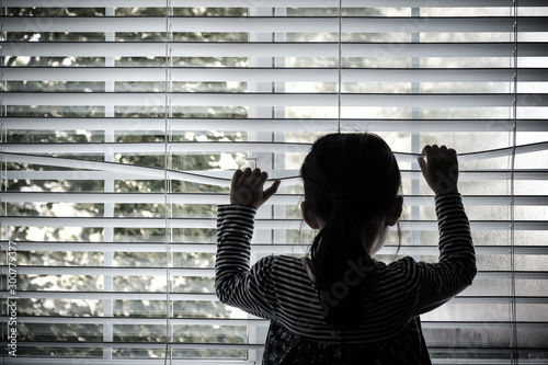 Fotografie Lonely toddler child standing in front of a window looking outside