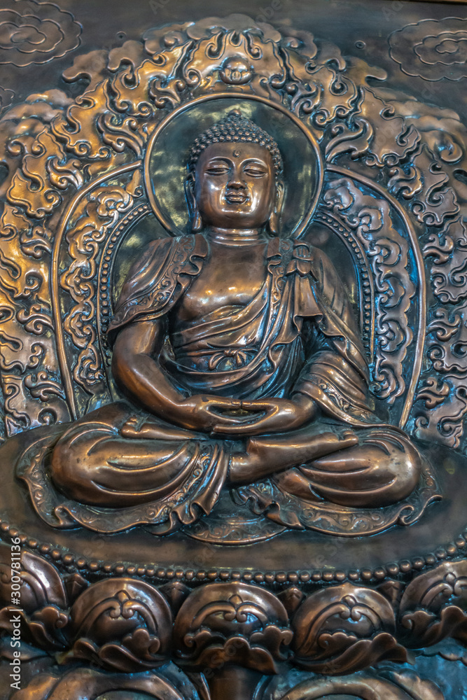 Da Nang, Vietnam - March 10, 2019: Chua An Long Chinese Buddhist Temple. Closeup of brass plated image of sitting Buddha in wall.