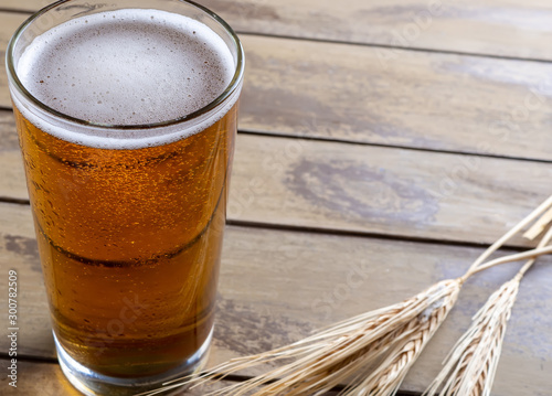 Glass of beer with ears of wheat on wooden background photo