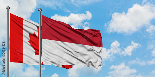 Canada and Indonesia flag waving in the wind against white cloudy blue sky together. Diplomacy concept, international relations.