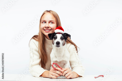 pretty young blond girl with her little cute dog wearing Santas red hat at Christmas holiday isolated on white background, lifestyle people concept