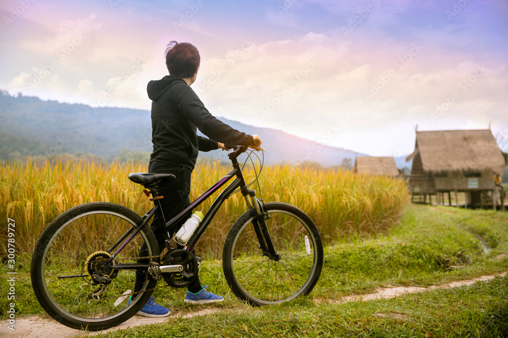 Obraz premium Woman standing with bike looking at rice field , Bike at the summer sunset in the nature. Bicycle and ecology lifestyle concept.