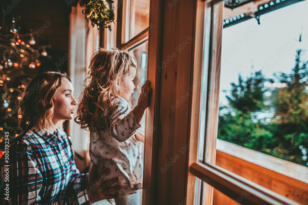 Mother and Daughter Having Fun on Christmas Morning. Precious family moment, young mom playing with her toddler daughter by decorated Christmas Tree and the window, winter landscape.  - obrazy, fototapety, plakaty 