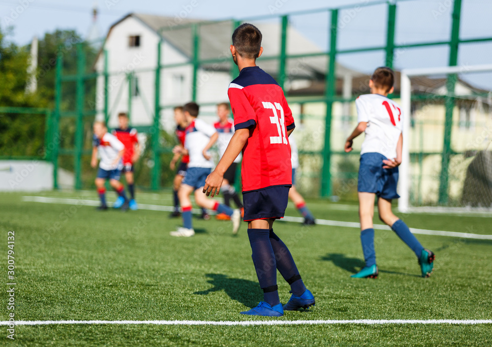 Obraz premium Boys in white and blue sportswear plays football on field, dribbles ball. Young soccer players with ball on green grass. Training, football, active lifestyle for kids concept 