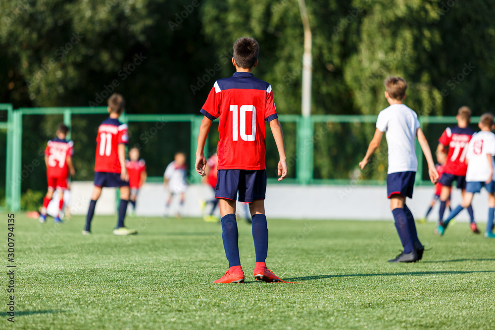 Obraz premium Boys in white and blue sportswear plays football on field, dribbles ball. Young soccer players with ball on green grass. Training, football, active lifestyle for kids concept