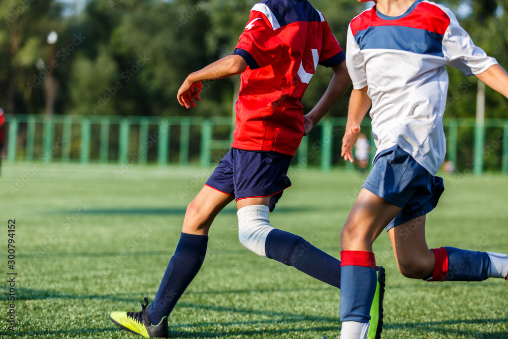 Boys in white and blue sportswear plays football on field, dribbles ball. Young soccer players with ball on green grass. Training, football, active lifestyle for kids concept Boys in white and blue sportswear plays football on field, dribbles ball. Young soccer players with ball on green grass. Training, football, active lifestyle for kids concept