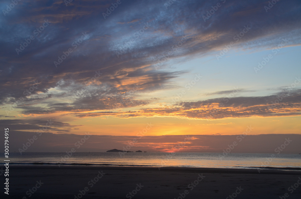 Dawn beauty, picturesque tropical orange coloured stratocumulus cloud coastal sunrise seascape in a blue sky.