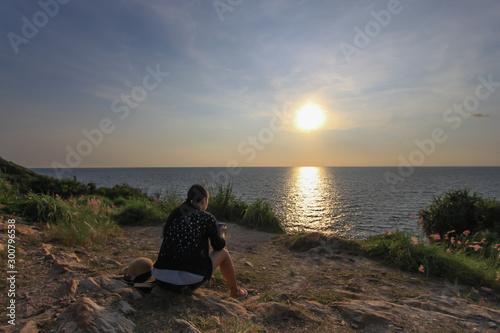 A young woman sitting alone on a cliff before the sun sets at Ko Samet Beach, Thailand © weerachai