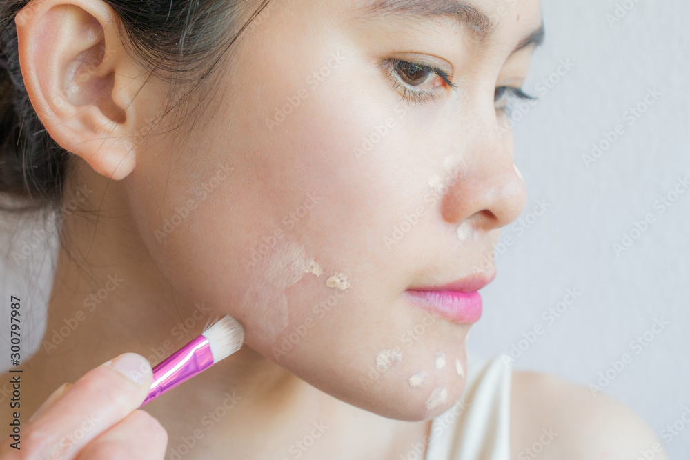 Closeup of Asian woman applying concealer on her facial skin with brush. Concealer is a type of cosmetic that is used to mask dark circles, age spots, large pores etc. Closeup of Asian woman applying concealer on her facial skin with brush. Concealer is a type of cosmetic that is used to mask dark circles, age spots, large pores etc.