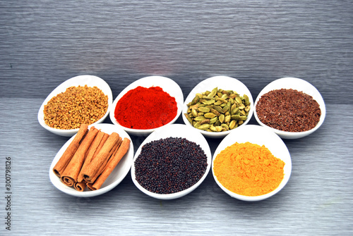 Healthy spices and herbs on gray background, fenugreek, chili powder, cardamom, flax seed, cinnamon, mustard seed, and turmeric