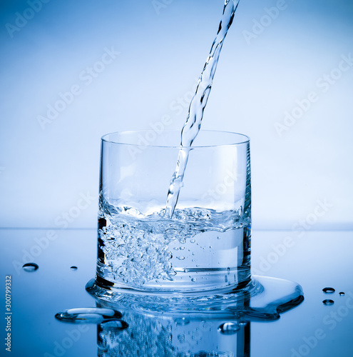 Pouring fresh pure water from bottle into a glass on the table with water drops, Healthcare and beauty hydration concept