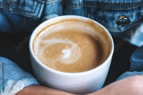 Closeup image of a woman holding a cup of hot latte coffee on the table