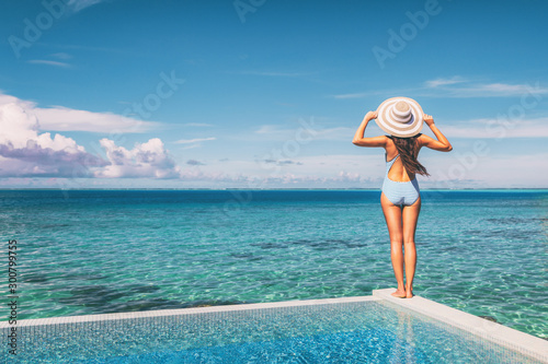 Beach vacation woman standing on infinity pool looking at blue turquoise ocean landscape with had and stripes bathing suit, vintage feel.