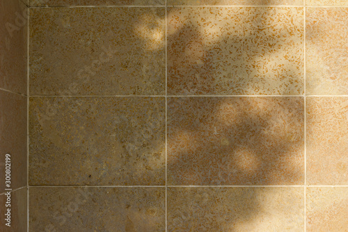 Natural stone tile wall texture background with tan color porous stone blocks, showing nearby tree shadows