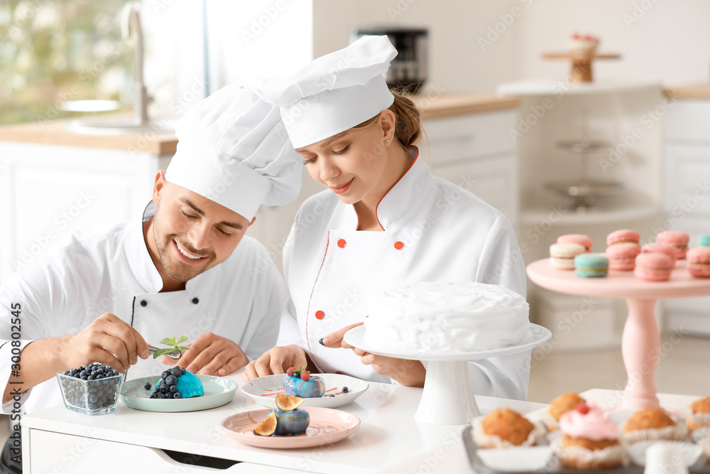 Young confectioners decorating tasty dessert in kitchen