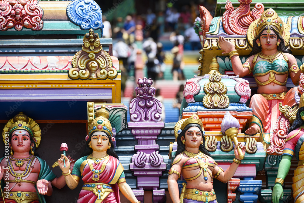 (Selective focus) Representation of Hindu gods and tourists climbing a colorful stairs leading to the Batu Caves in the background. Kuala Lumpur, Malaysia