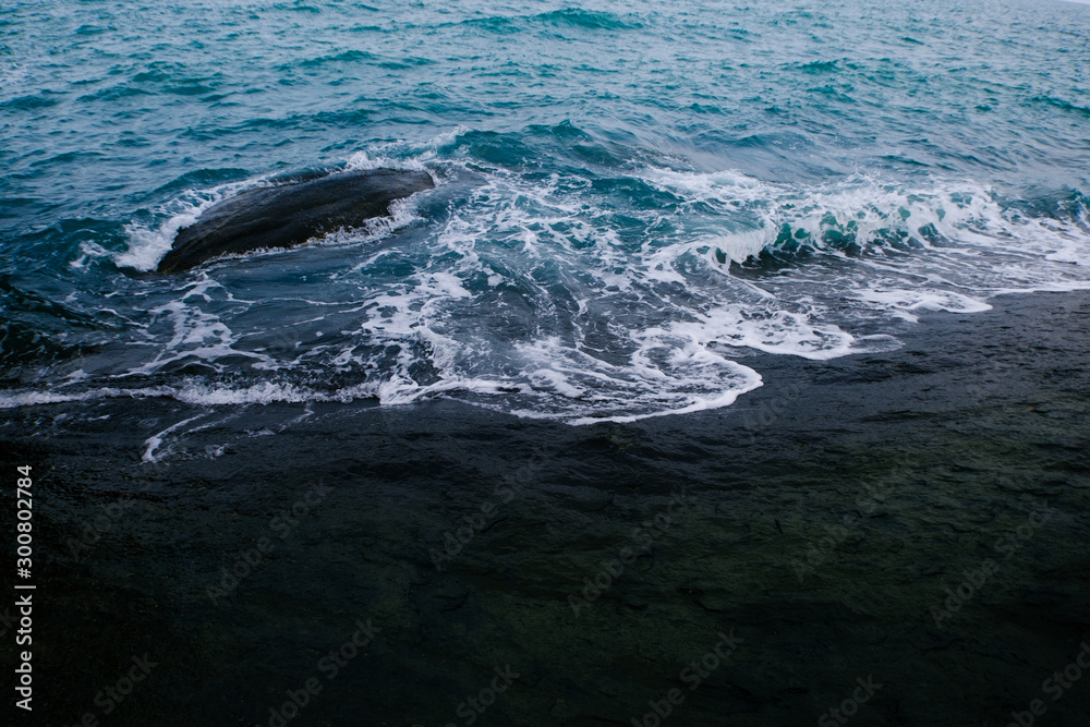 Naklejka premium Dark blue sea wave crashing near a rocky shore