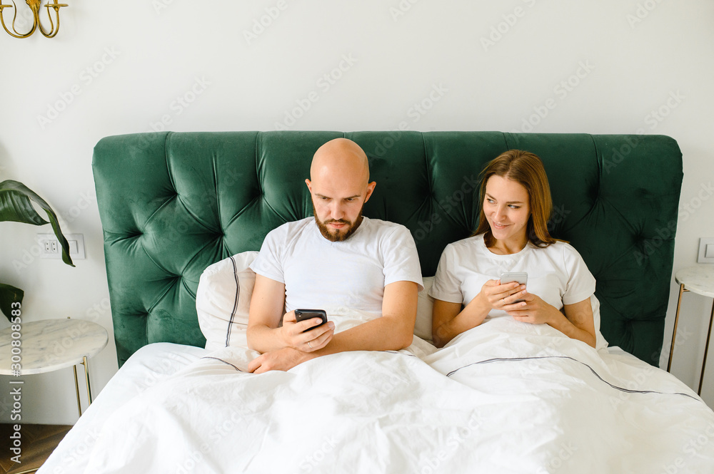 young couple lie in bed with phones. Communication and relationship problems. young couple lie in bed with phones. Communication and relationship problems.