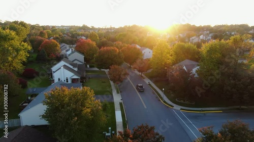 Pick up truck turns onto street through residential neighborhood community, colorful autumn fall leaves line the road, evening glow or warm sunset photo