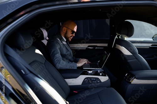 businessman working on laptop in back seat of Executive car. Concept of business, success, traveling, luxury.