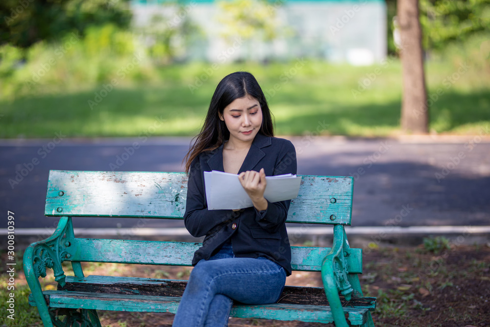 women sitting on bench in park reading paper women sitting on bench in park reading paper