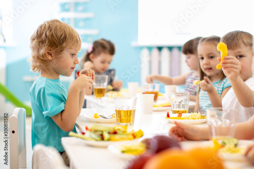Group of children have dinner. Kids eating healthy food in kindergarten.