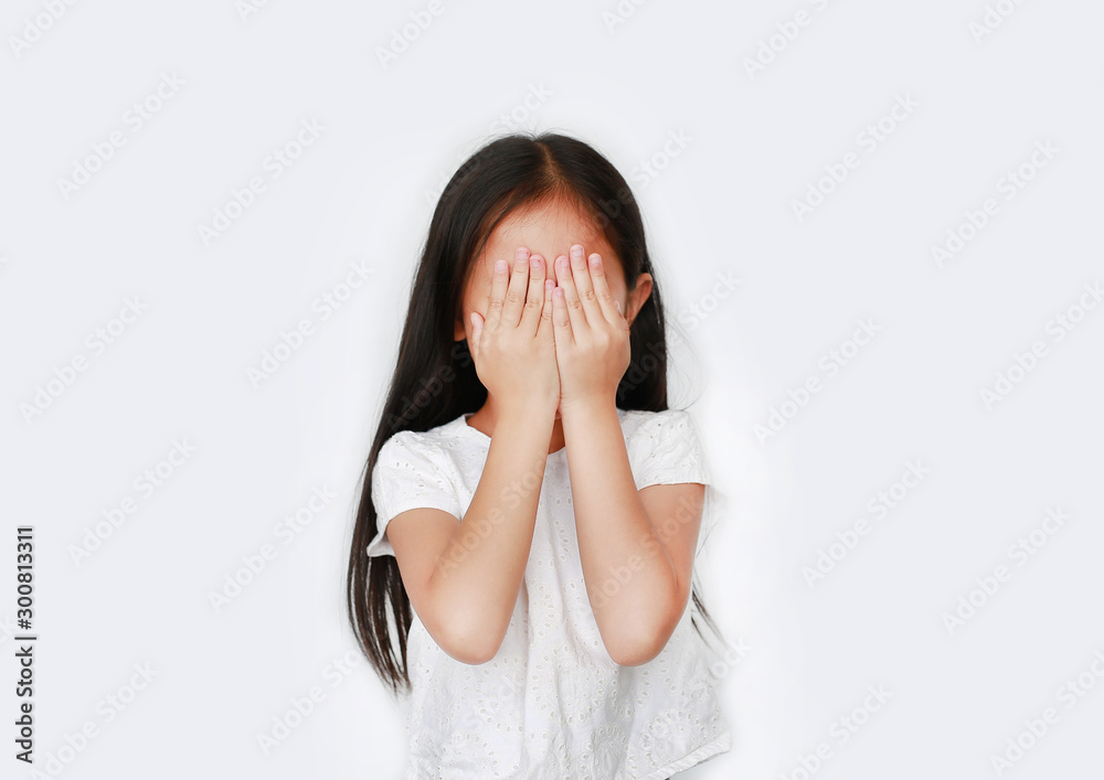 Portrait of little Asian girl closing hid eyes by hand isolated on white background. Kid is crying and rubbing her eyes with her hands.