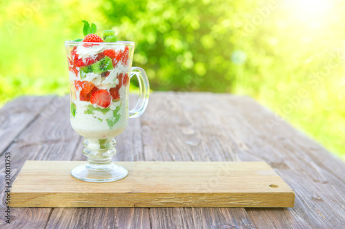 layered dessert with strawberries and cream cheese on wooden table over green garden background photo