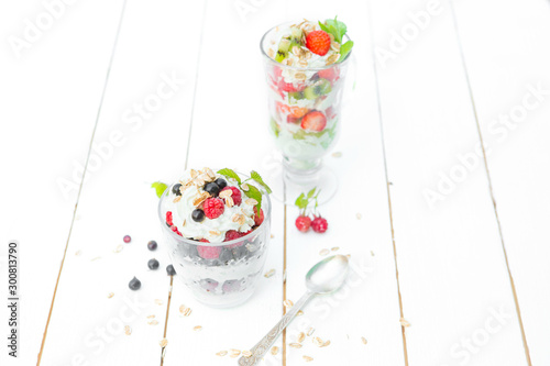Layered dessert with raspberry, strawberry, black currant and kiwi, cream and biscuits in glasses