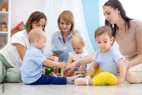 Group of toddlers and their mothers playing with colorful educational toys in nursery room